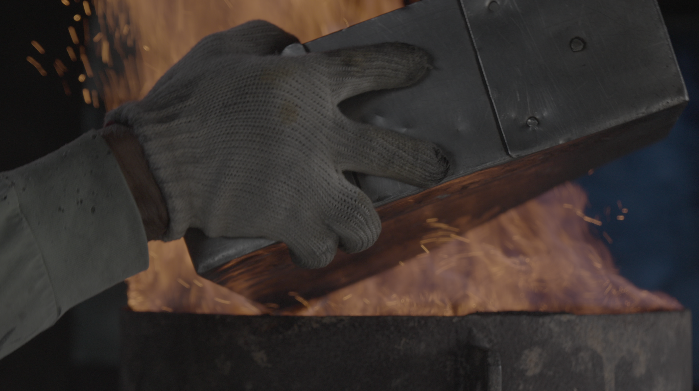 Gloved hands working steel above the fire